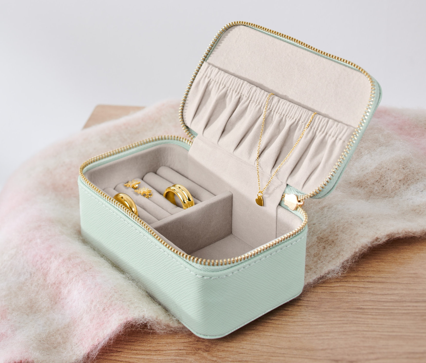 Otwarta kasetka na biżuterię z pierścionkami, kolczykami i naszyjnikiem.