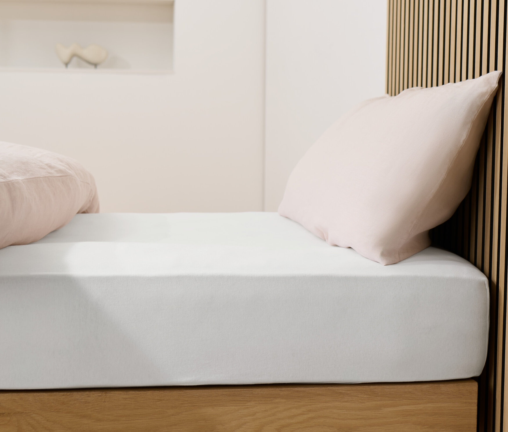 Łóżko z białym prześcieradłem dżersejowym i różowymi poduszkami.