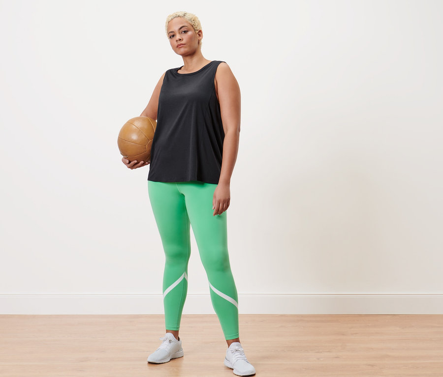Kobieta trzyma piłkę do siatkówki, ma na sobie zielone legginsy sportowe i antracytowy top sportowy.