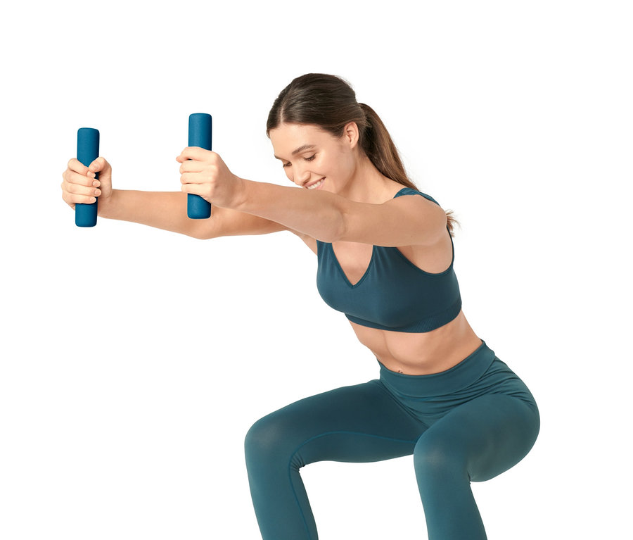 Kobieta robi przysiady z niebieskimi ciężarkami, 2 sztuki, w dłoniach.