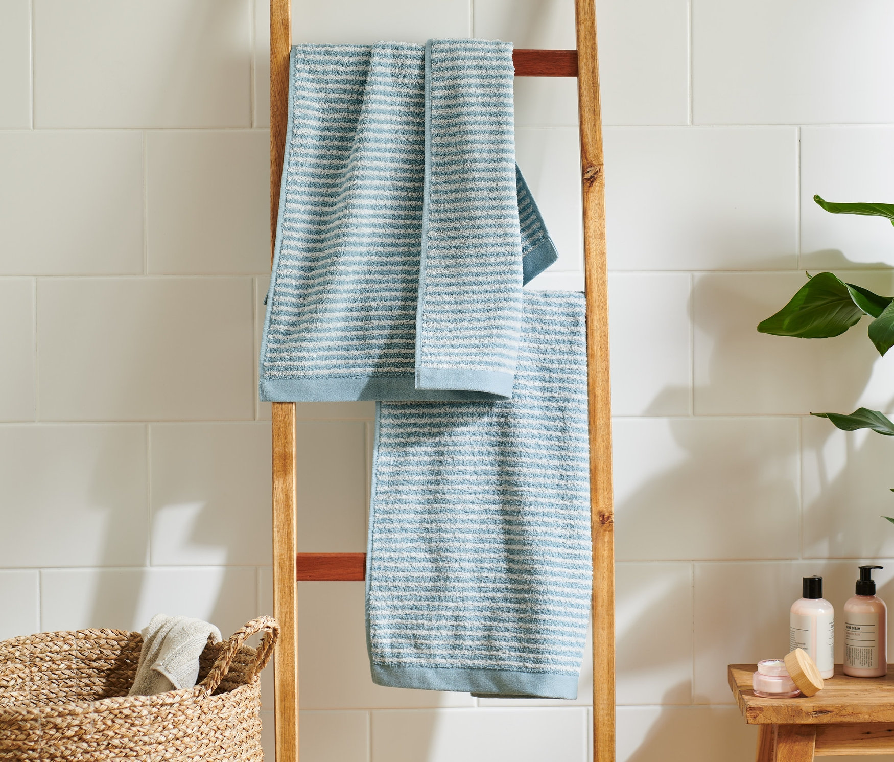 Dwa wysokiej jakości ręczniki w kolorach błękitnym i niebieskim wiszą na drewnianej drabinie w łazience.