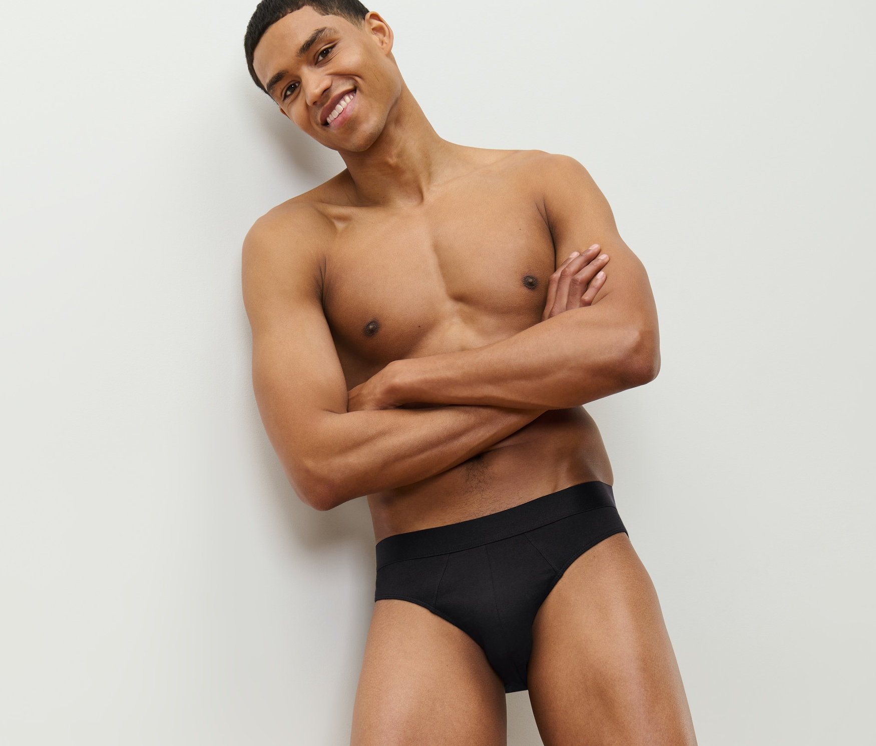 Uśmiechnięty mężczyzna pozuje z założonymi rękami na piersi i ma na sobie czarne slipy, 4 pary.