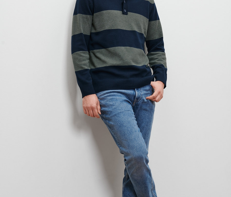 Mężczyzna oparty o ścianę ma na sobie sweter w paski i dżinsy.