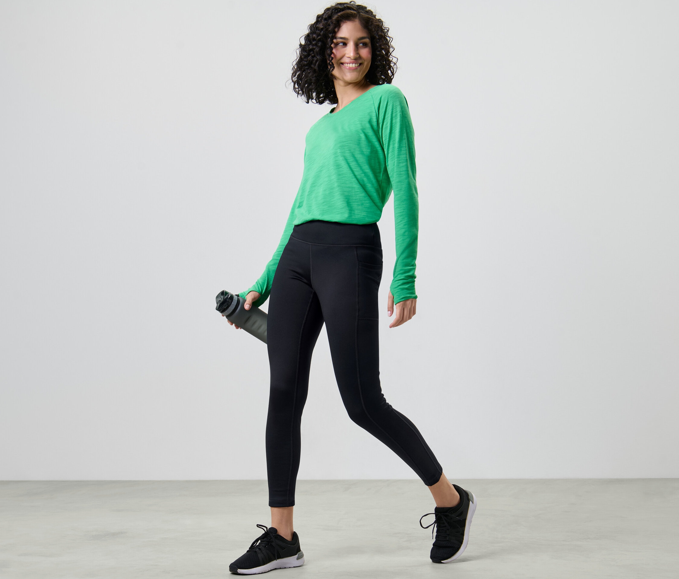 Kobieta w zielonej koszulce i legginsach termoaktywnych trzyma butelkę z wodą.