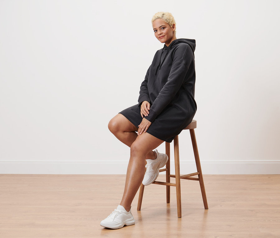 Kobieta siedzi na stołku i ma na sobie sukienkę dresową z kapturem.