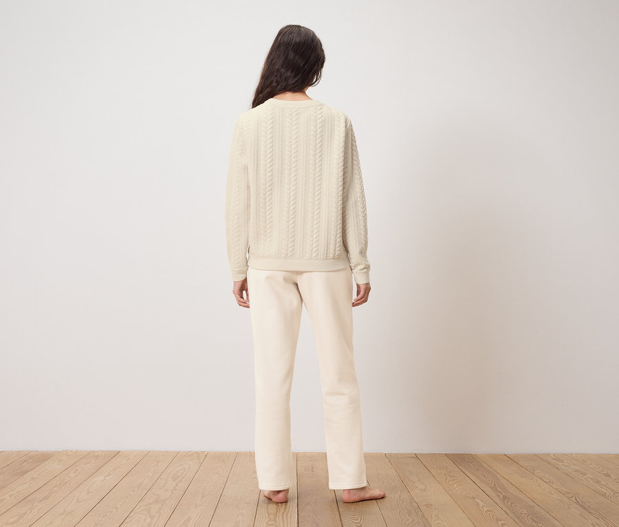 Kobieta stoi tyłem do kamery, ubrana w kremowy sweter i spodnie.