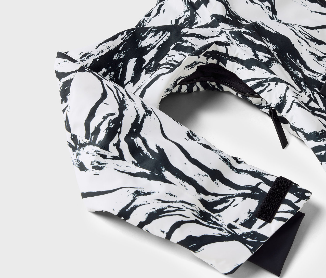 Zbliżenie na białą kurtkę z czarnym wzorem, widoczny rękaw i zamek błyskawiczny.