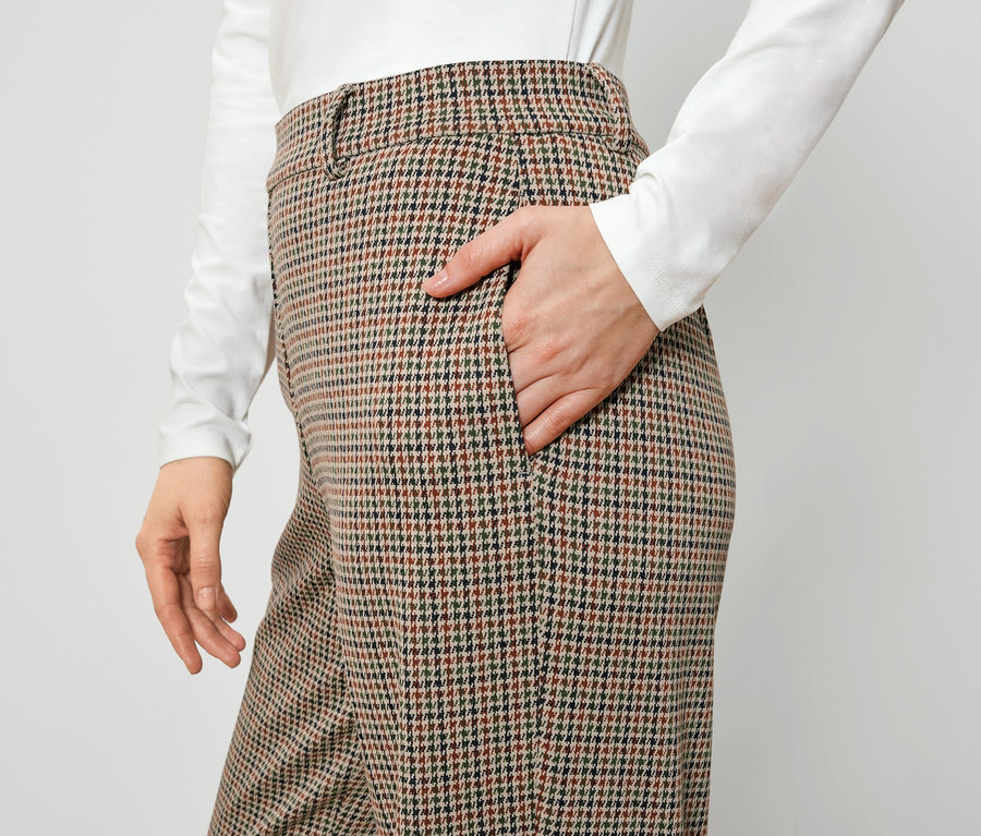 Kobieta trzyma rękę w kieszeni brązowych spodni w kratę.