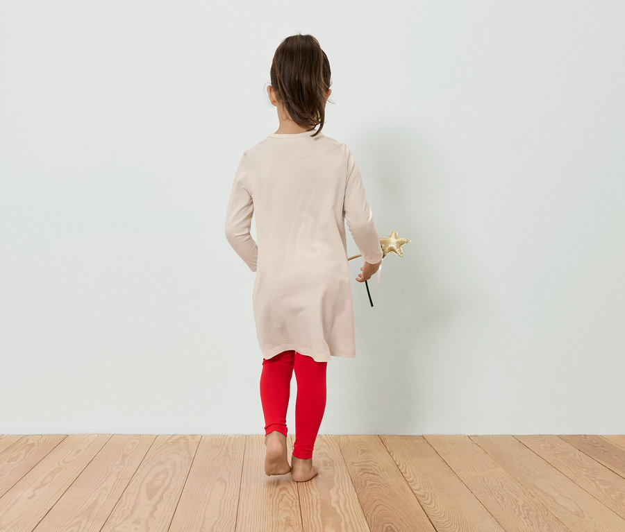 Dziewczynka w sukience i legginsach trzyma w ręku gwiazdę, stojąc tyłem do kamery.