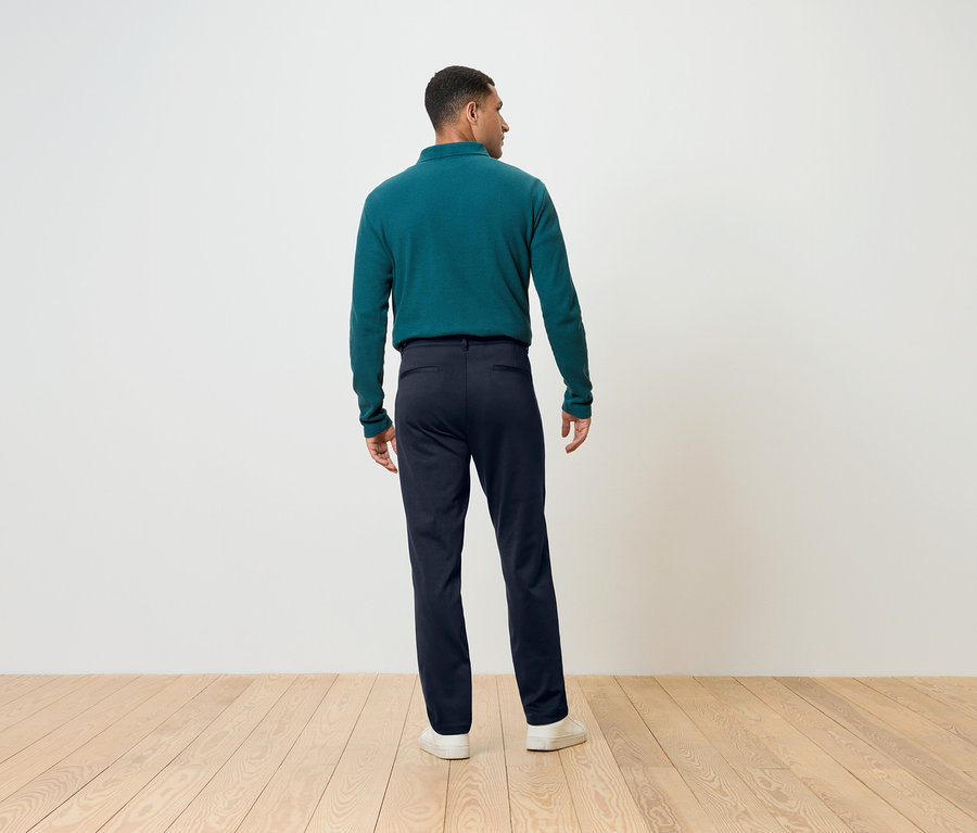 Mężczyzna odwrócony tyłem ma na sobie niebieskie spodnie i zielony top z długim rękawem.