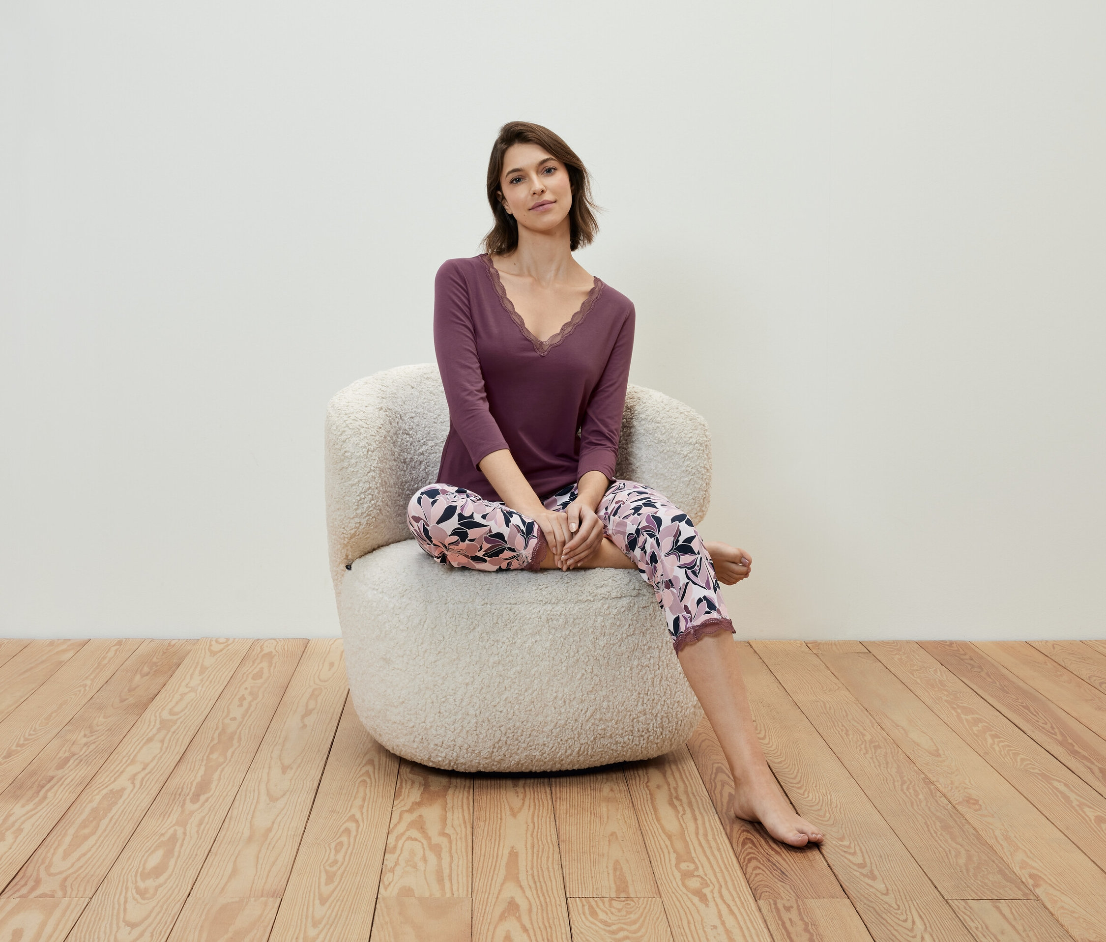 Kobieta siedzi w fotelu, ubrana w fioletową koszulkę i spodnie w kwiaty.