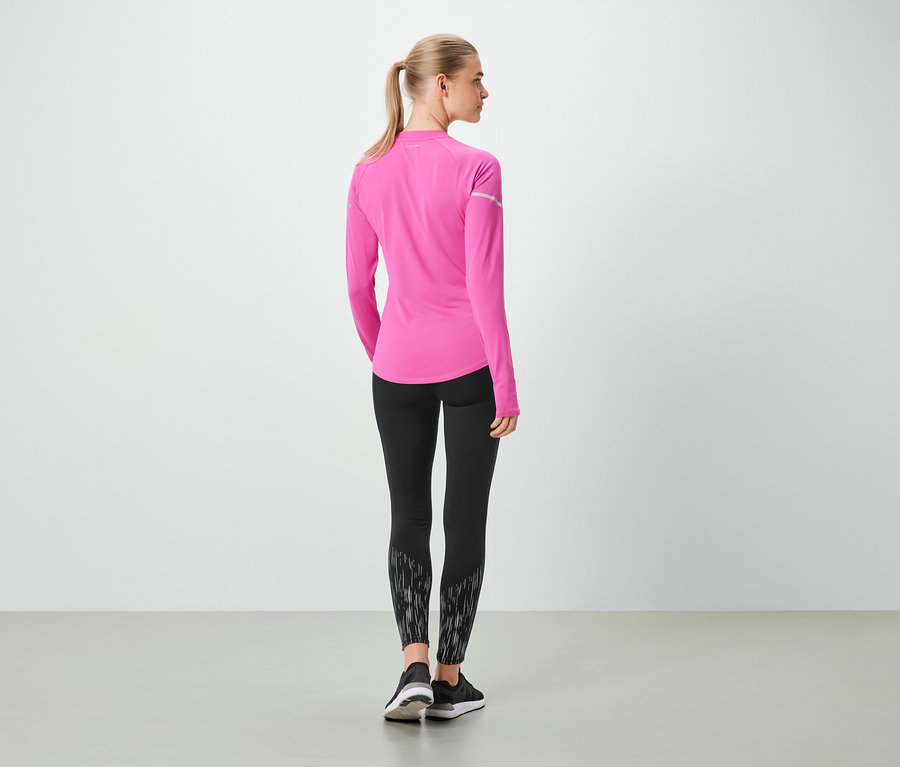 Kobieta tyłem do kamery ma na sobie różowy top z długim rękawem i czarne legginsy.