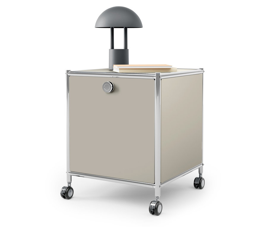 Na górze beżowej szafki na kółkach stoi szara lampa i książka.