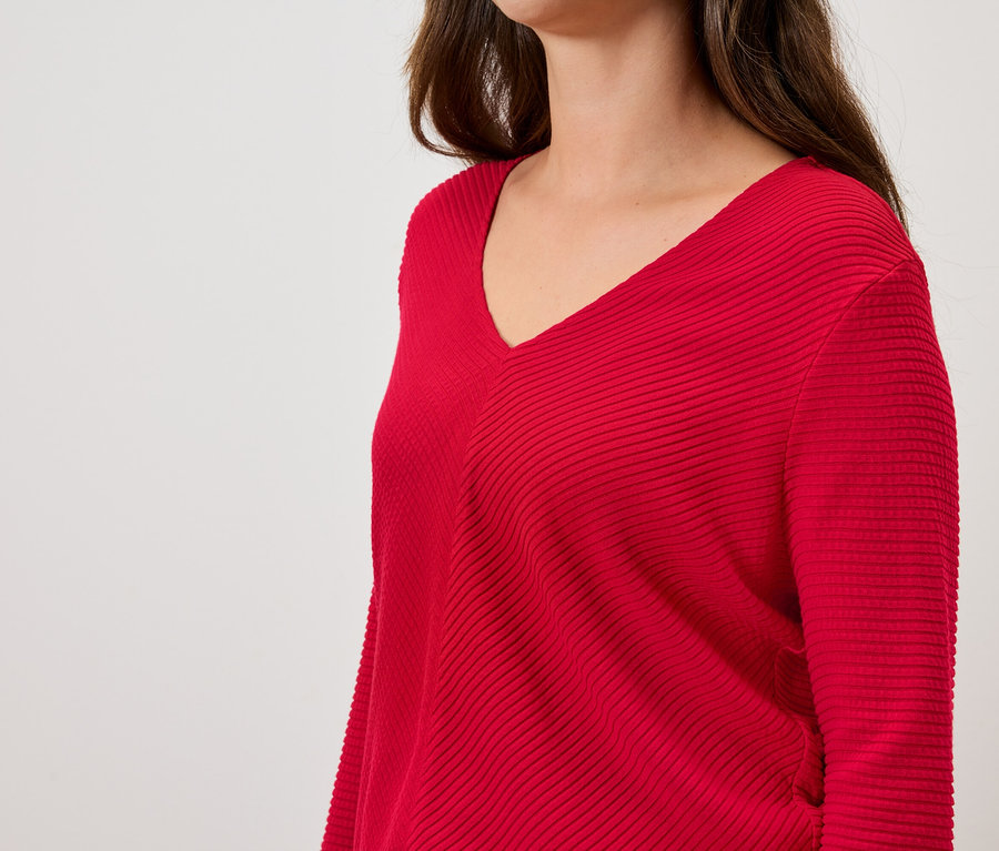 Kobieta ma na sobie czerwony sweter z długimi rękawami i dekoltem w serek.