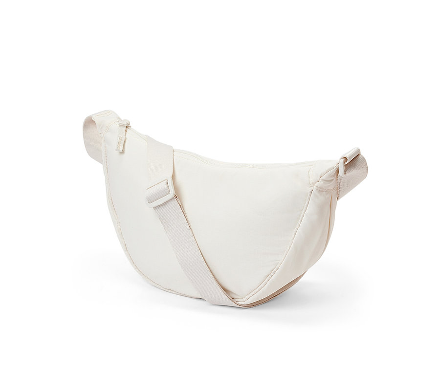 Kremowa torebka na ramię leży na białym tle.