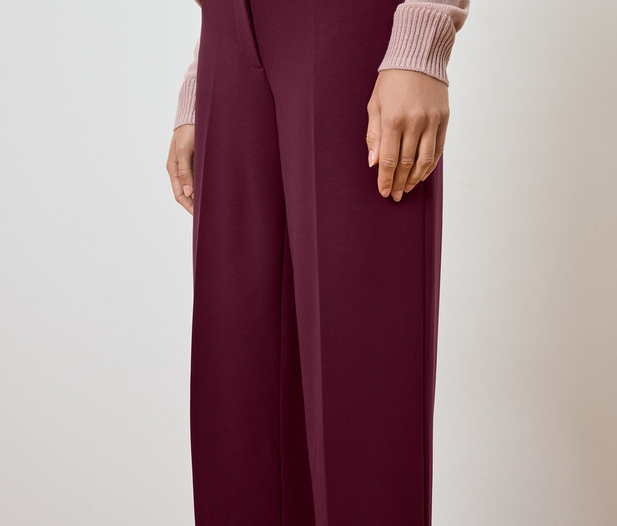 Częściowy widok osoby ubranej w bordowe spodnie i jasnoróżowy sweter.