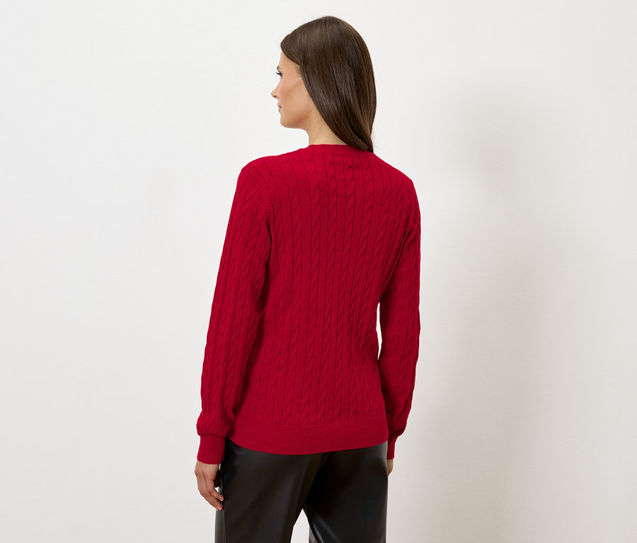 Kobieta stoi tyłem, ubrana w czerwony sweter i czarne skórzane spodnie.