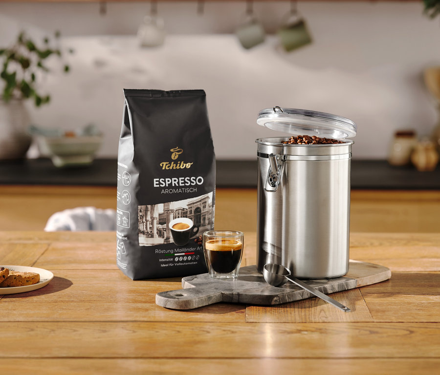 Opakowanie espresso stoi obok otwartej puszki zatrzymującej zapach ze stali nierdzewnej i filiżanki na drewnianym stole.