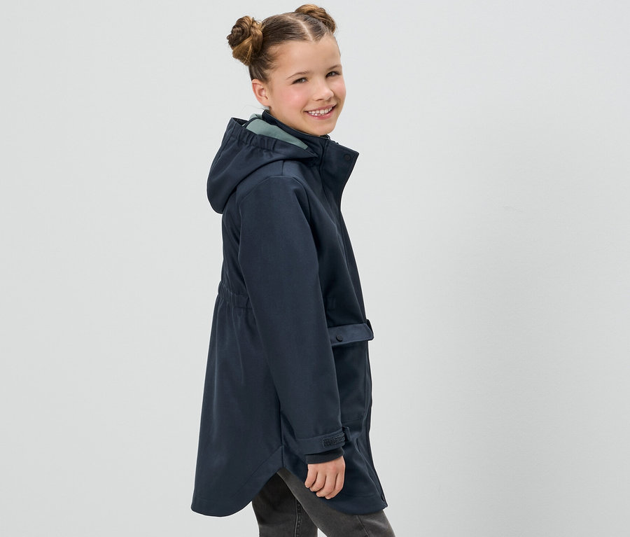 Uśmiechnięta dziewczyna pozuje w granatowym softshellu dziecięcym i szarych dżinsach.