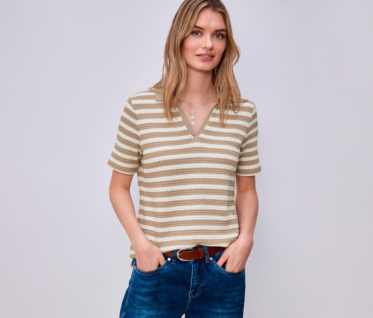 Kobieta w dżinsach i brązowym pasku ma na sobie koszulkę z dzianiny Street One w paski z dekoltem w serek.