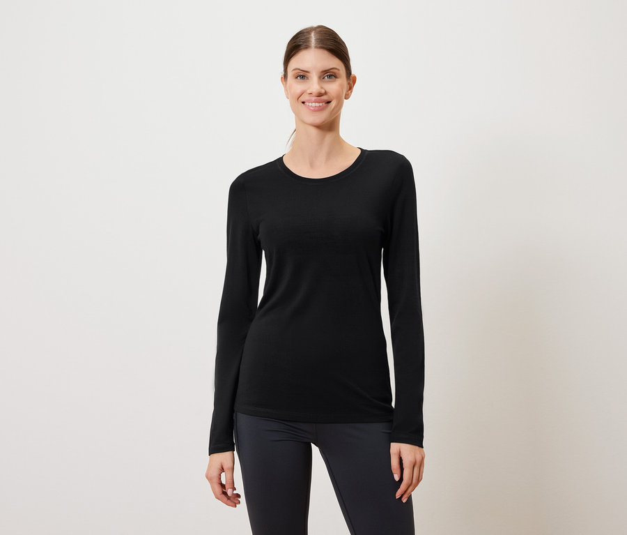 Kobieta ma na sobie czarną koszulę z długim rękawem i ciemne legginsy na białym tle.