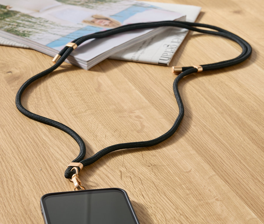 Czarny łańcuszek do telefonu z złotymi detalami leży na stole obok magazynu i beżowej torebki.