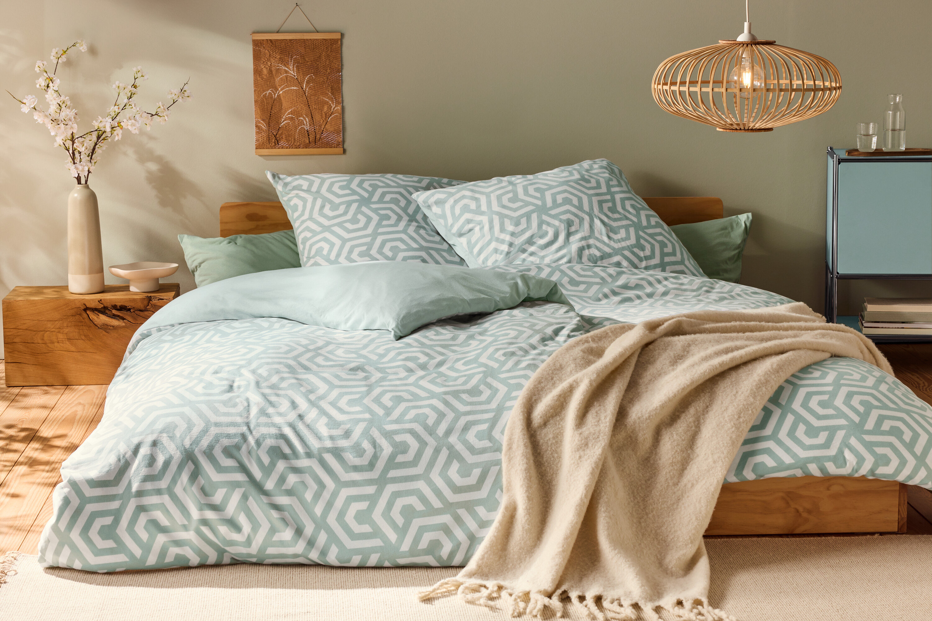 Łóżko z pościelą z dżerseju w standardowym rozmiarze, z geometrycznym wzorem i jasnozielonymi poduszkami.