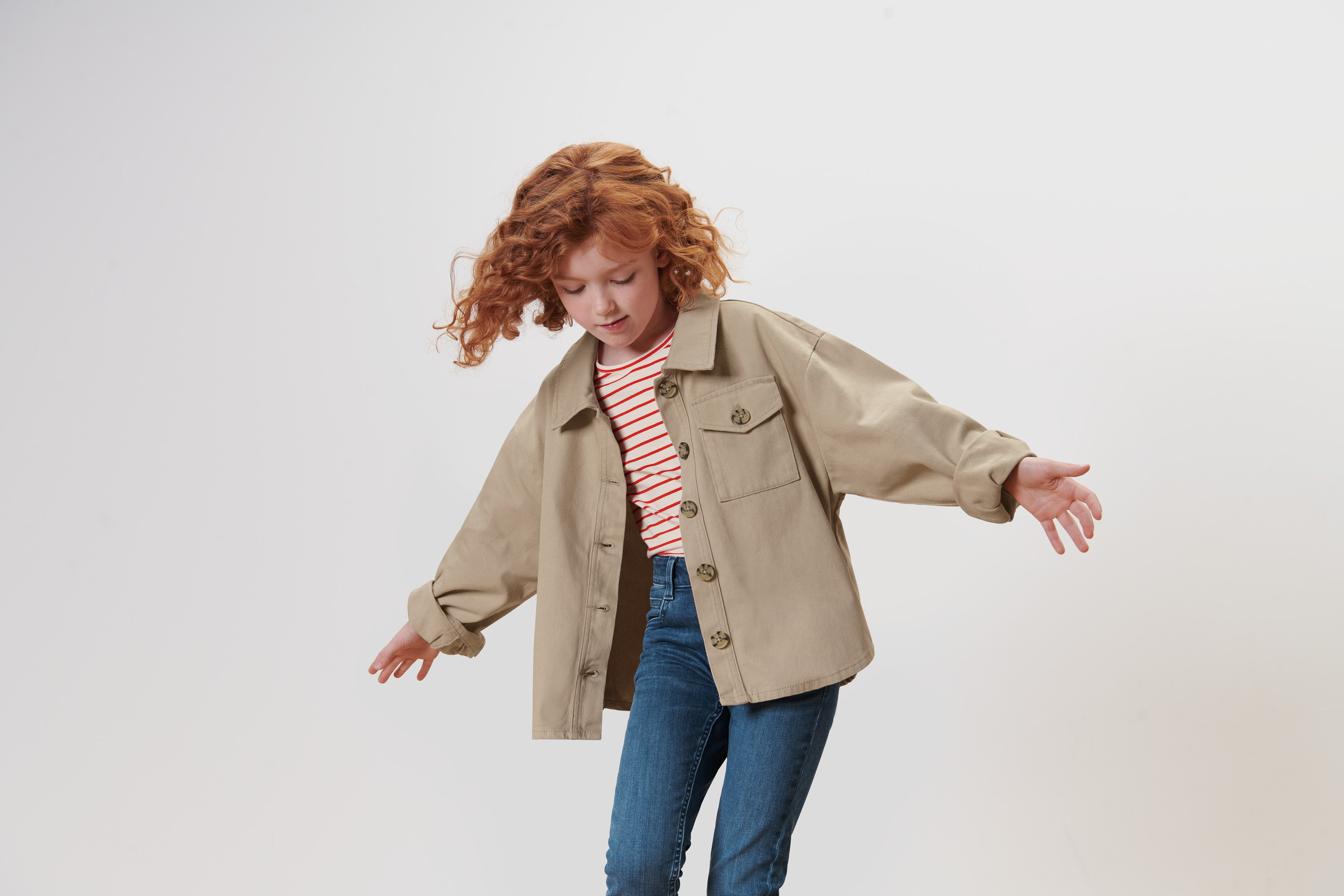 Ruda, kręcona dziewczyna macha rękami, ubrana w kurtkę dżinsową.