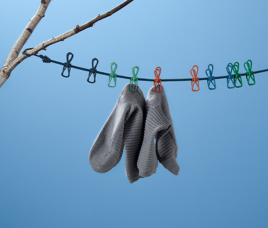 Dwie szare skarpetki wiszą na podróżnej lince do suszenia prania, przymocowanej do gałęzi drzewa na tle błękitnego nieba.