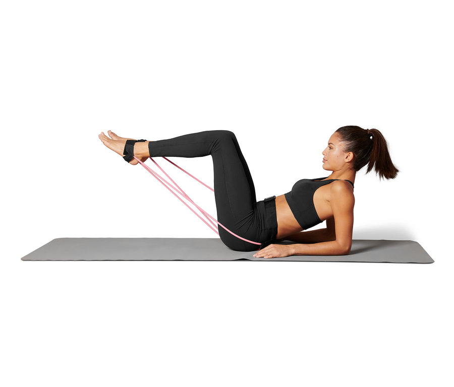 Kobieta leży na macie i ćwiczy z gumami do fitnessu przymocowanymi do nóg.