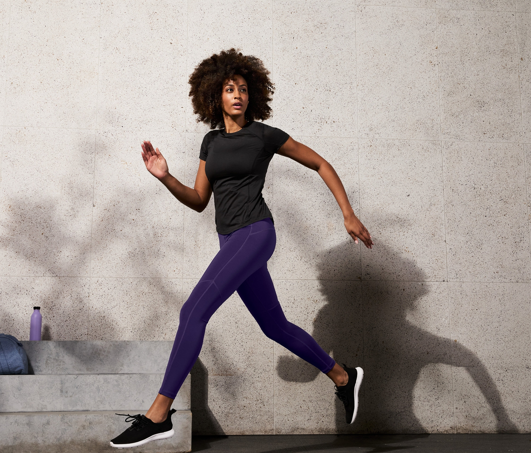 Kobieta biegnie w czarnej koszulce sportowej i modelujących legginsach sportowych.