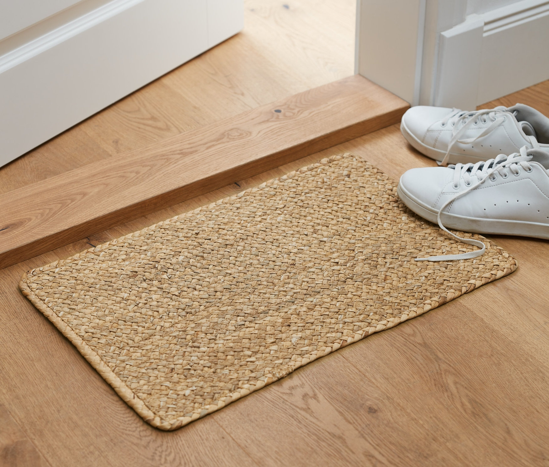 Przed otwartymi drzwiami leży dywan z hiacyntu wodnego, obok stoją buty.