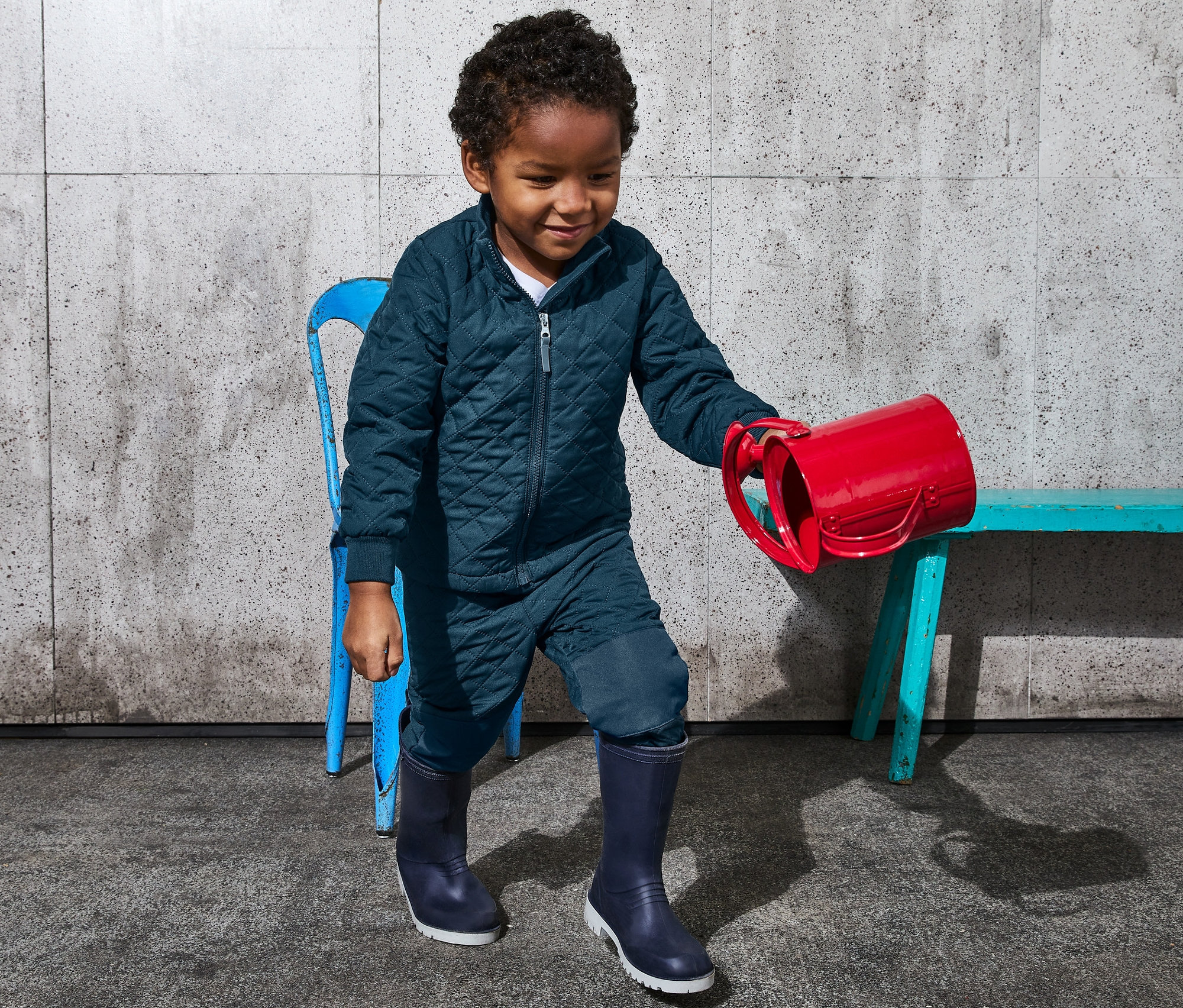 Chłopiec w zestawie pikowanym z materiału z recyklingu trzyma czerwony garnek.