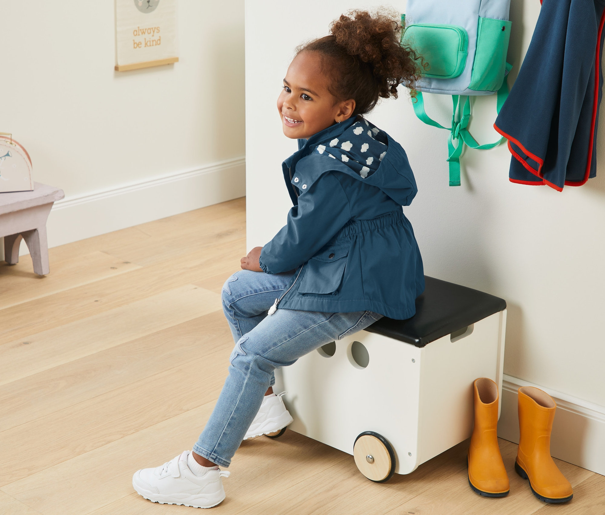 Dziewczynka siedzi na skrzyni z zabawkami i ma na sobie parkę.