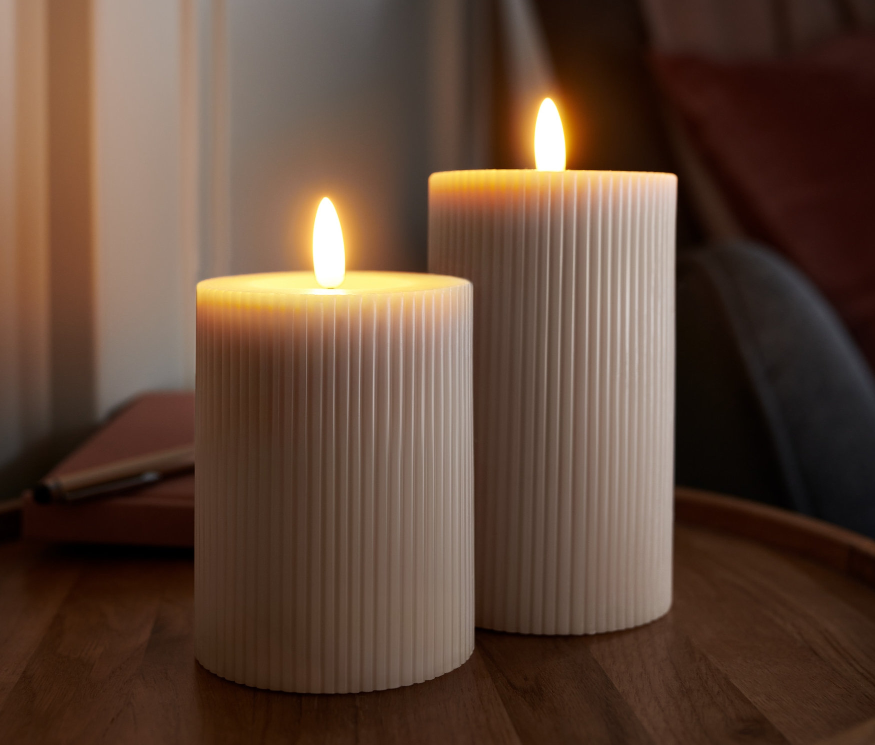 Dwie świece LED z prawdziwego wosku o prążkowanej teksturze stoją na drewnianym stoliku.