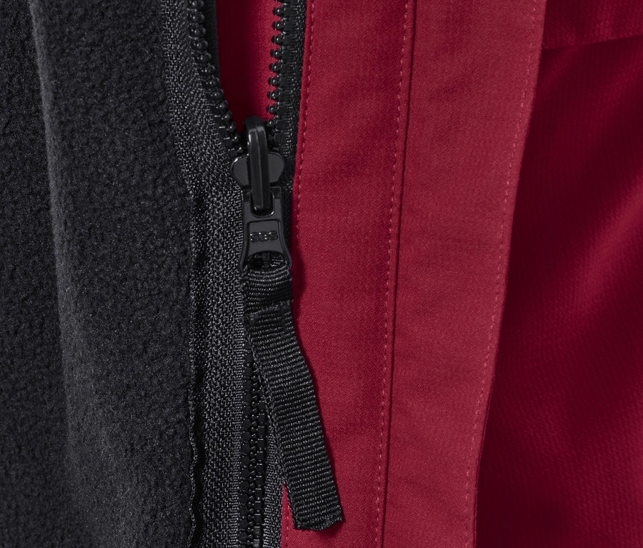 Zbliżenie na zamek błyskawiczny kurtki outdoorowej z czarną podszewką polarową i czerwonym materiałem zewnętrznym.