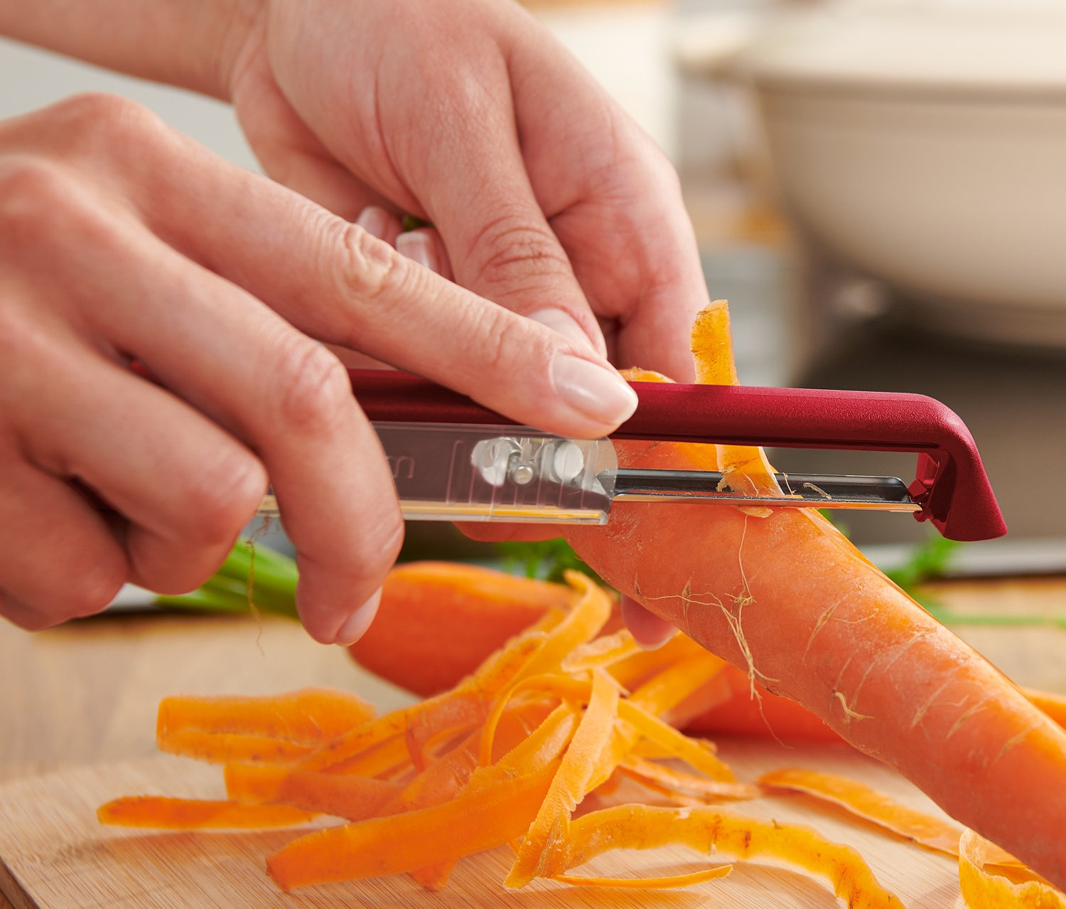 Osoba obiera marchewkę samostrzącym się nożem uniwersalnym na drewnianej desce.