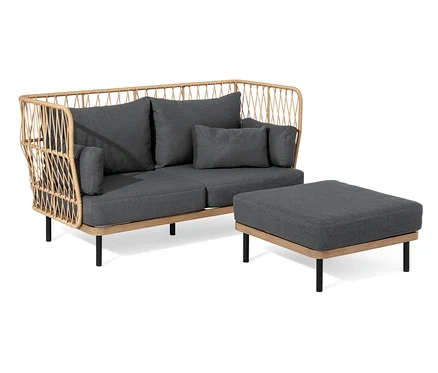 Rattanowa sofa z szarymi poduszkami i podnóżkiem.