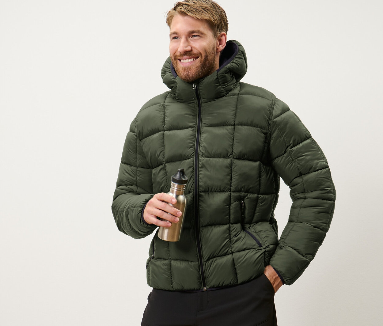 Mężczyzna trzyma butelkę z wodą i ma na sobie kurtkę pikowaną khaki.