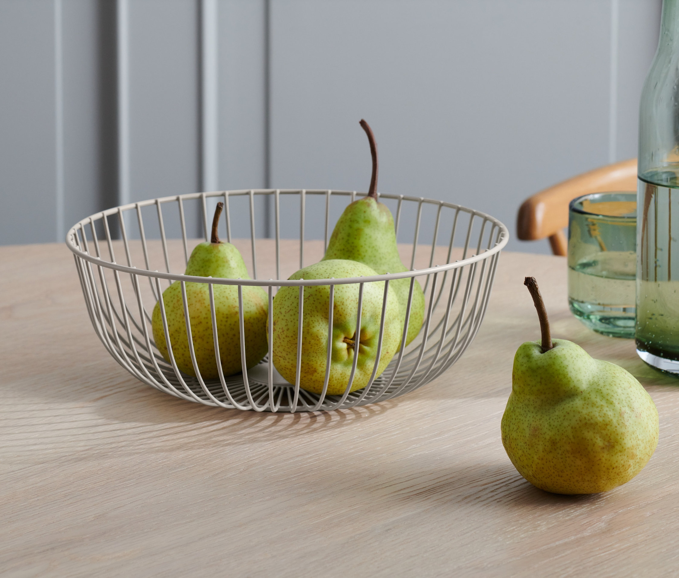 Trzy gruszki w misce drucianej i jedna obok na stole.