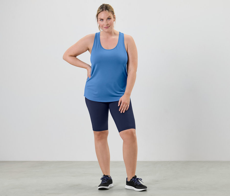 Kobieta pozuje w błękitnym topie funkcyjnym z dwuczęściowego zestawu i szortach kolarskich.