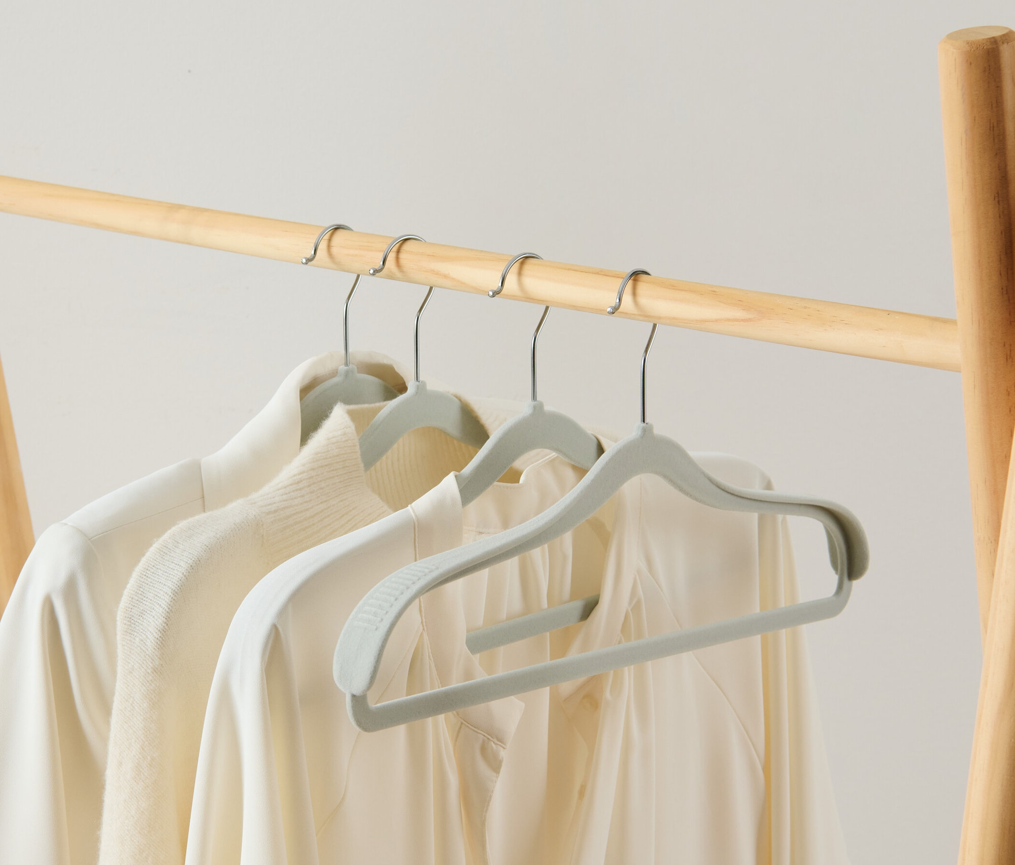 Na drewnianym wieszaku wiszą trzy Wieszaki na ubrania z pogrubioną okolicą ramion, 4 sztuki, na których wisi biała odzież.