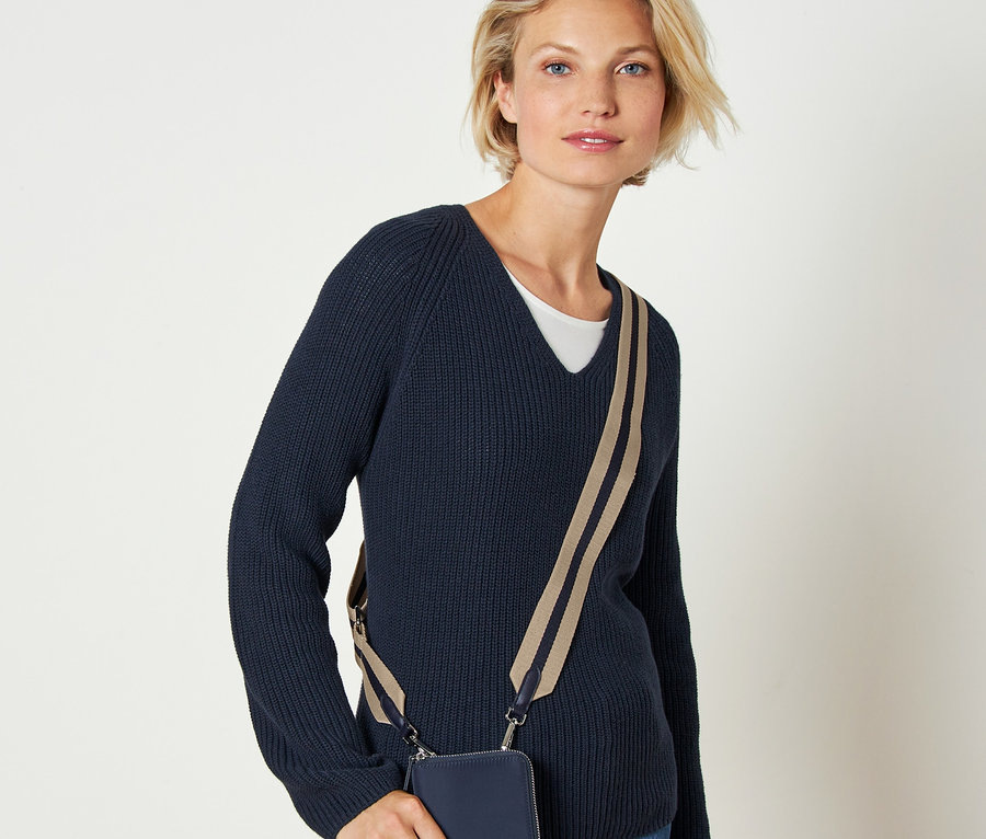 Blondynka w granatowym swetrze z wymiennym paskiem do torebki przewieszonym przez ciało.