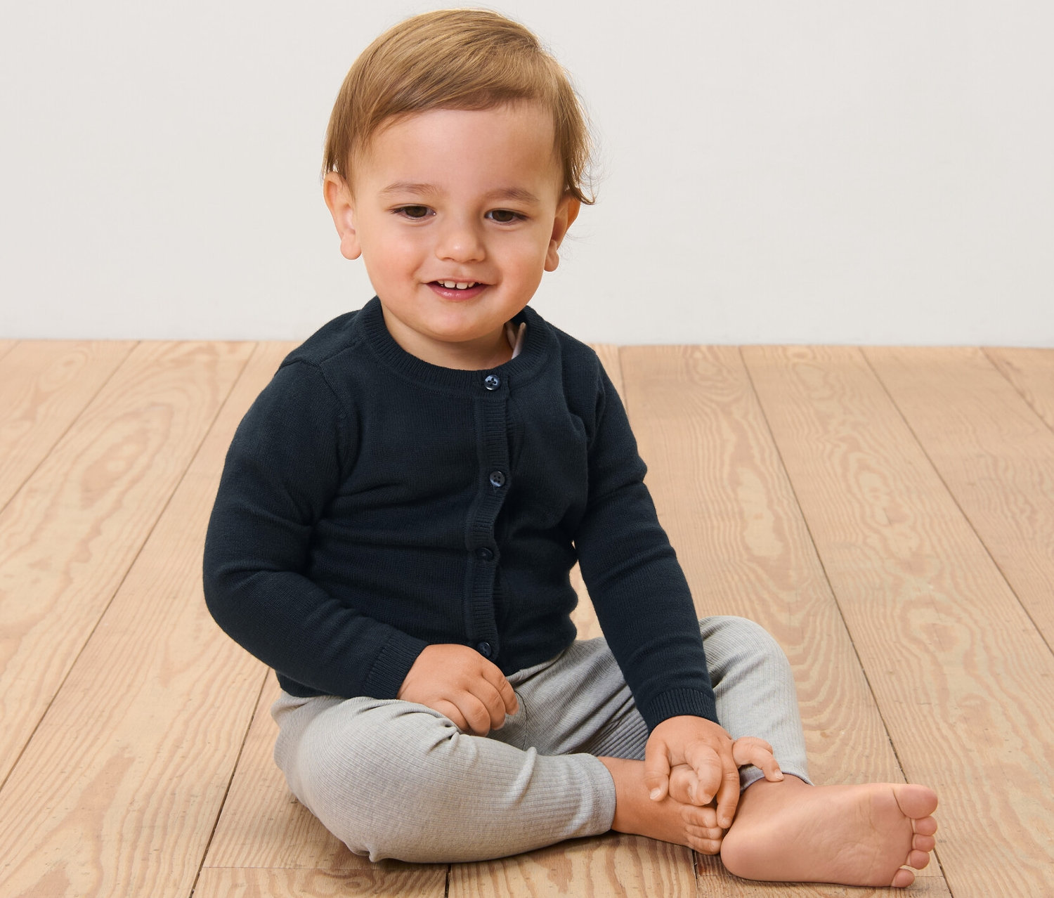 Dziecko siedzi na drewnianej podłodze i ma na sobie sweter rozpinany.