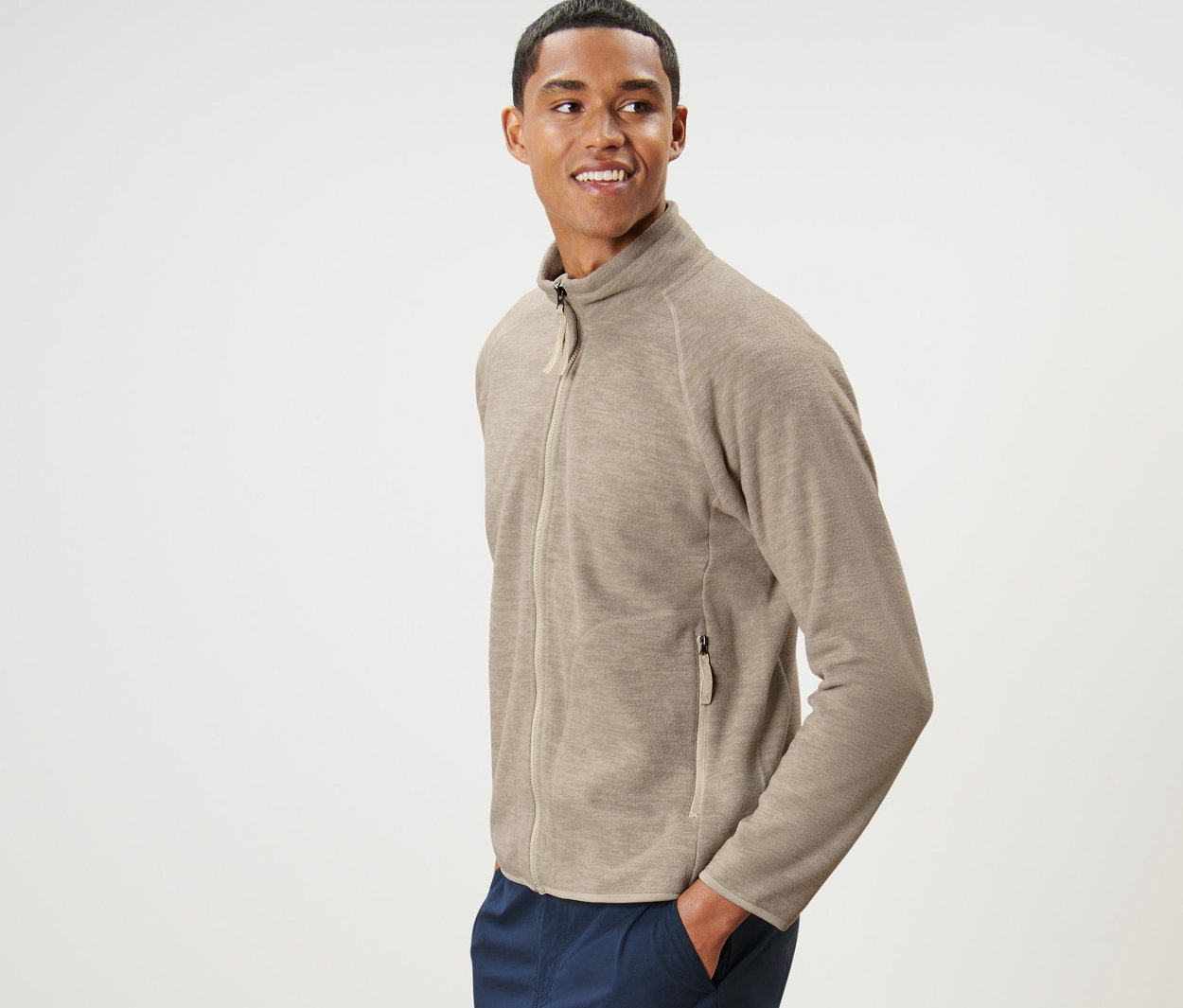 Mężczyzna pozuje w beżowej bluzie polarowej i granatowych spodniach.