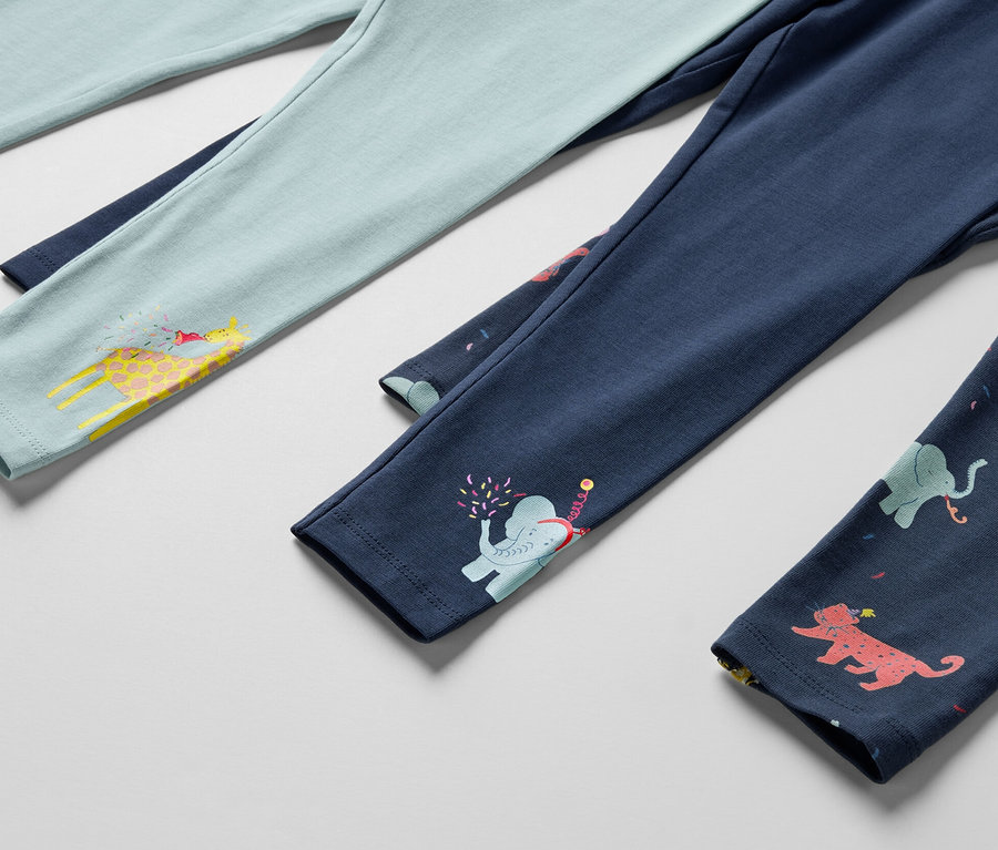 Szczegół trzech par legginsów dziecięcych, jedne jasnoniebieskie z żyrafą, jedne granatowe ze słoniem i jedne granatowe ze zwierzętami.