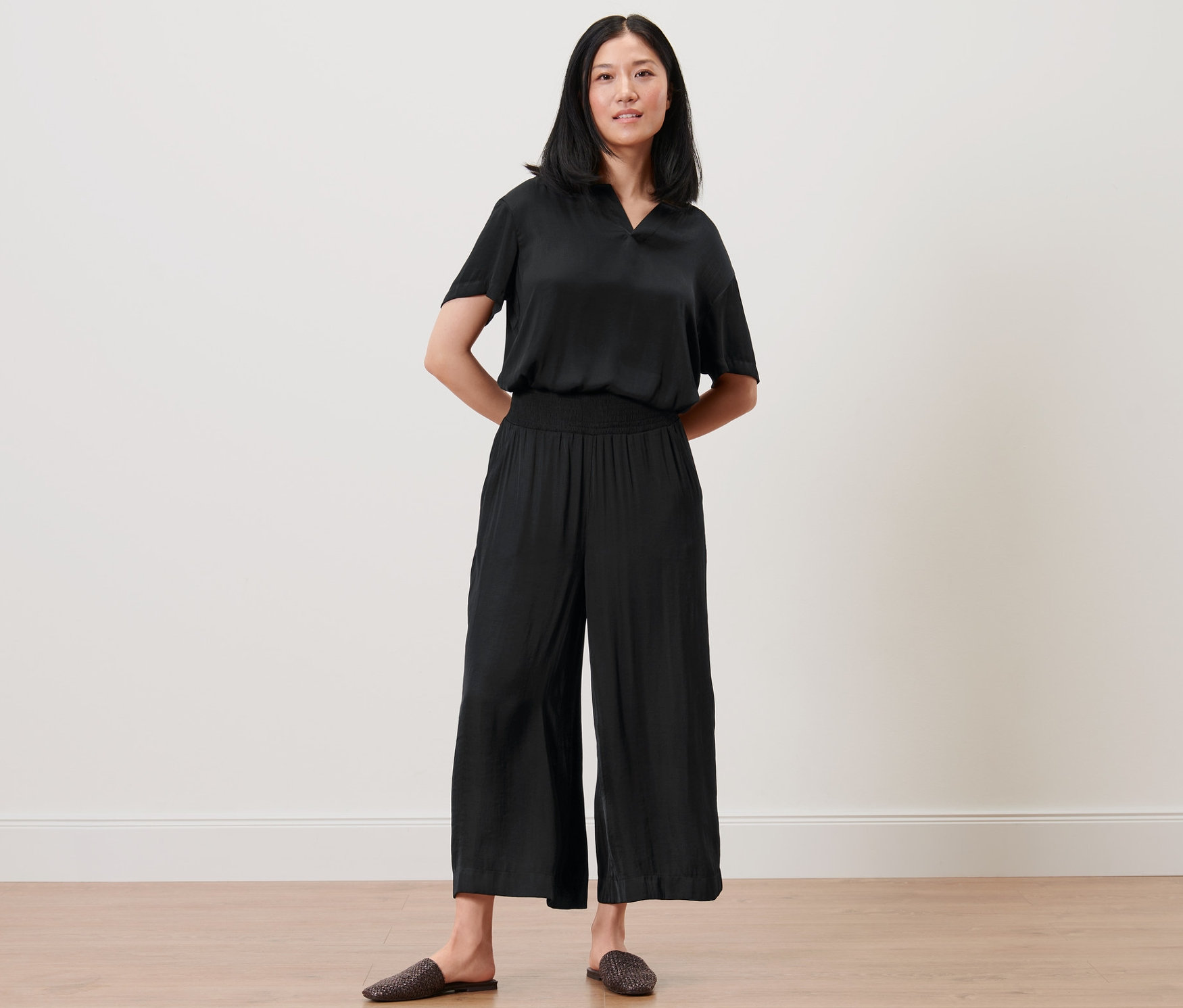 Kobieta pozuje w czarnych satynowych kulotach i topie.