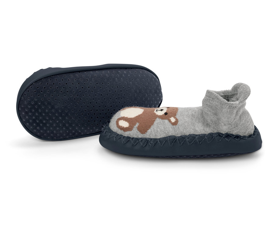 Szary kapcie dziecięce z misiem leżą obok granatowej podeszwy antypoślizgowej.