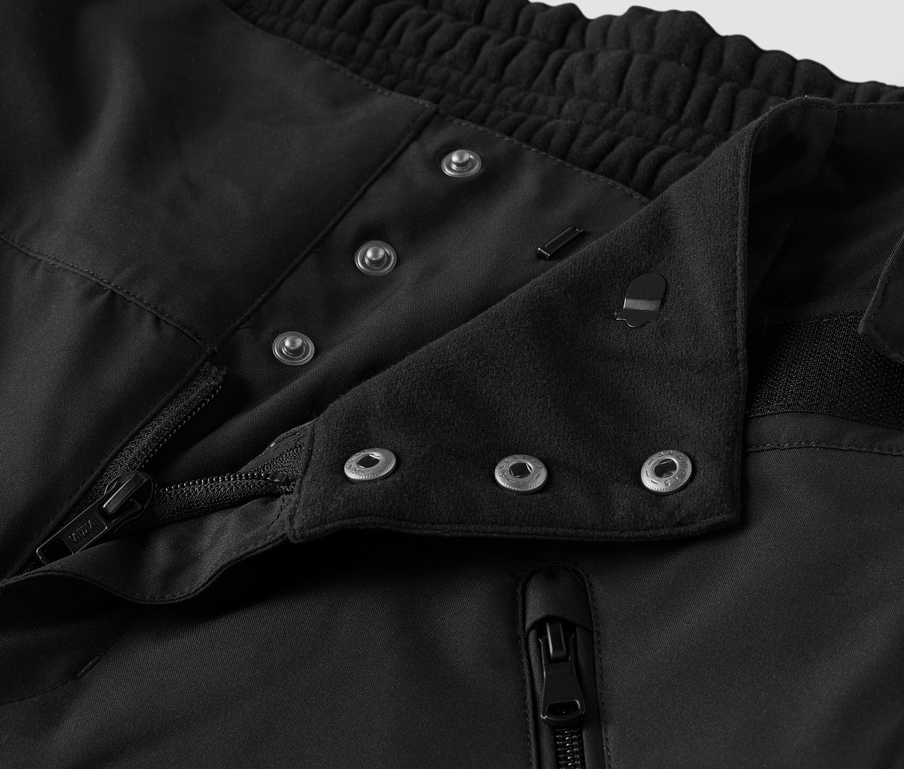 Zbliżenie czarnej tkaniny z guzikami i zamkiem błyskawicznym.