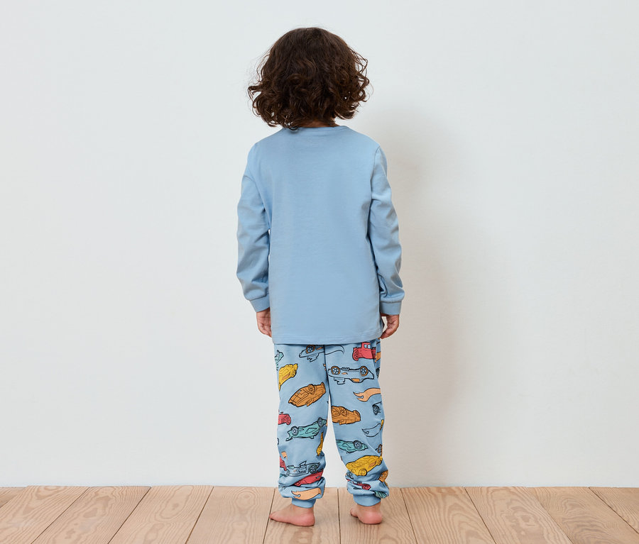 Dziecko tyłem do kamery ma na sobie niebieską piżamę z nadrukiem małych samochodów.